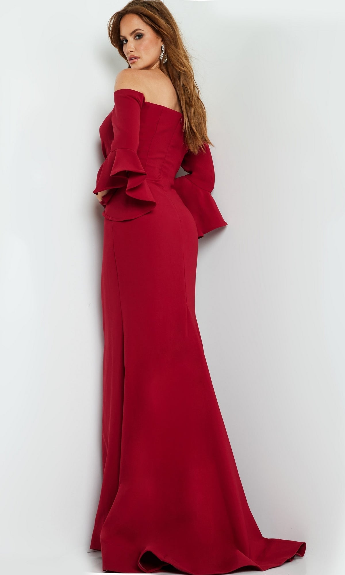 A woman in a fitted, off-the-shoulder Jovani 07065 Bell-Sleeve Designer Evening Gown stands facing away, looking over her shoulder.